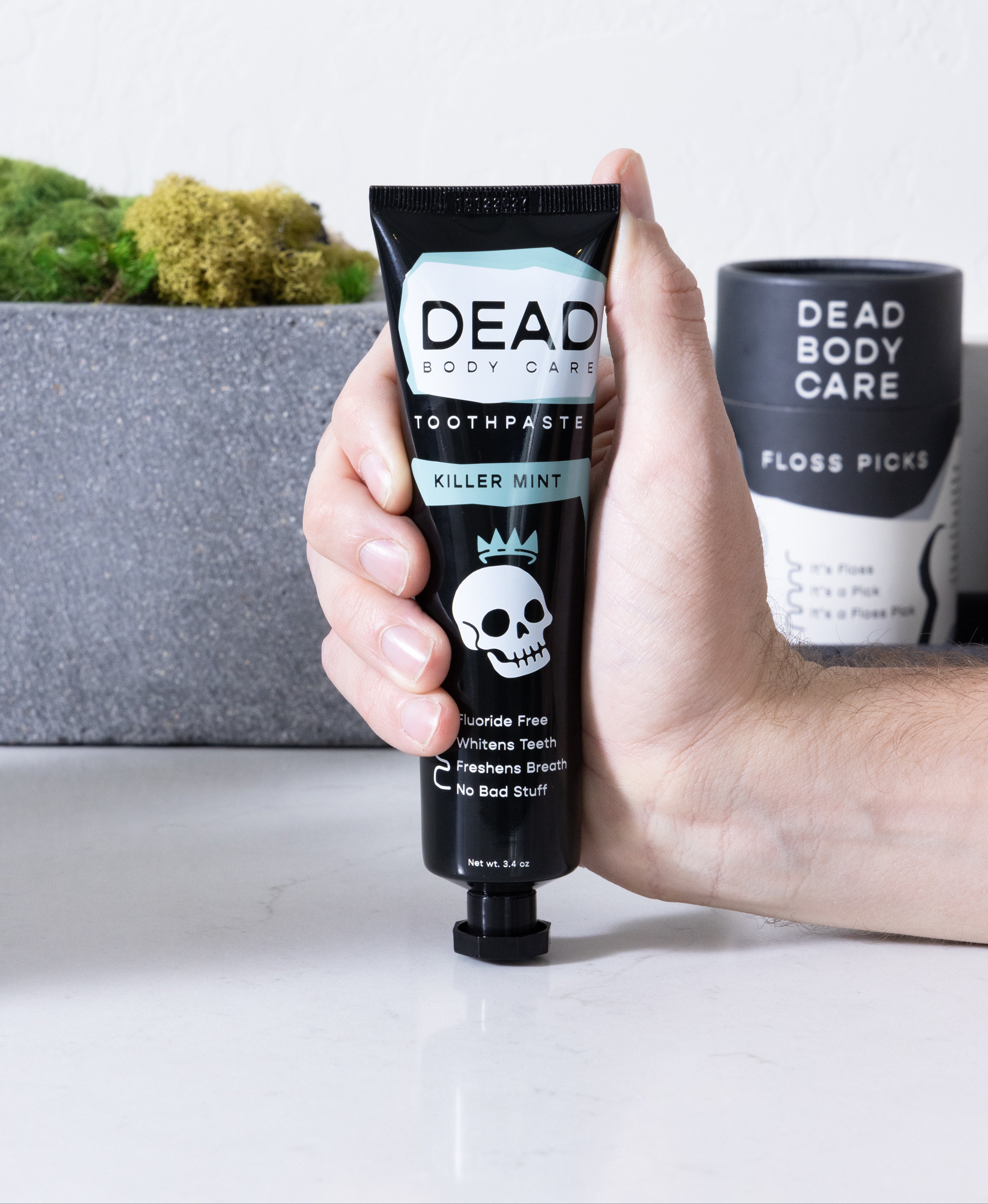Hand holding a tube of Dead Body Care toothpaste with a skull design on a white surface.